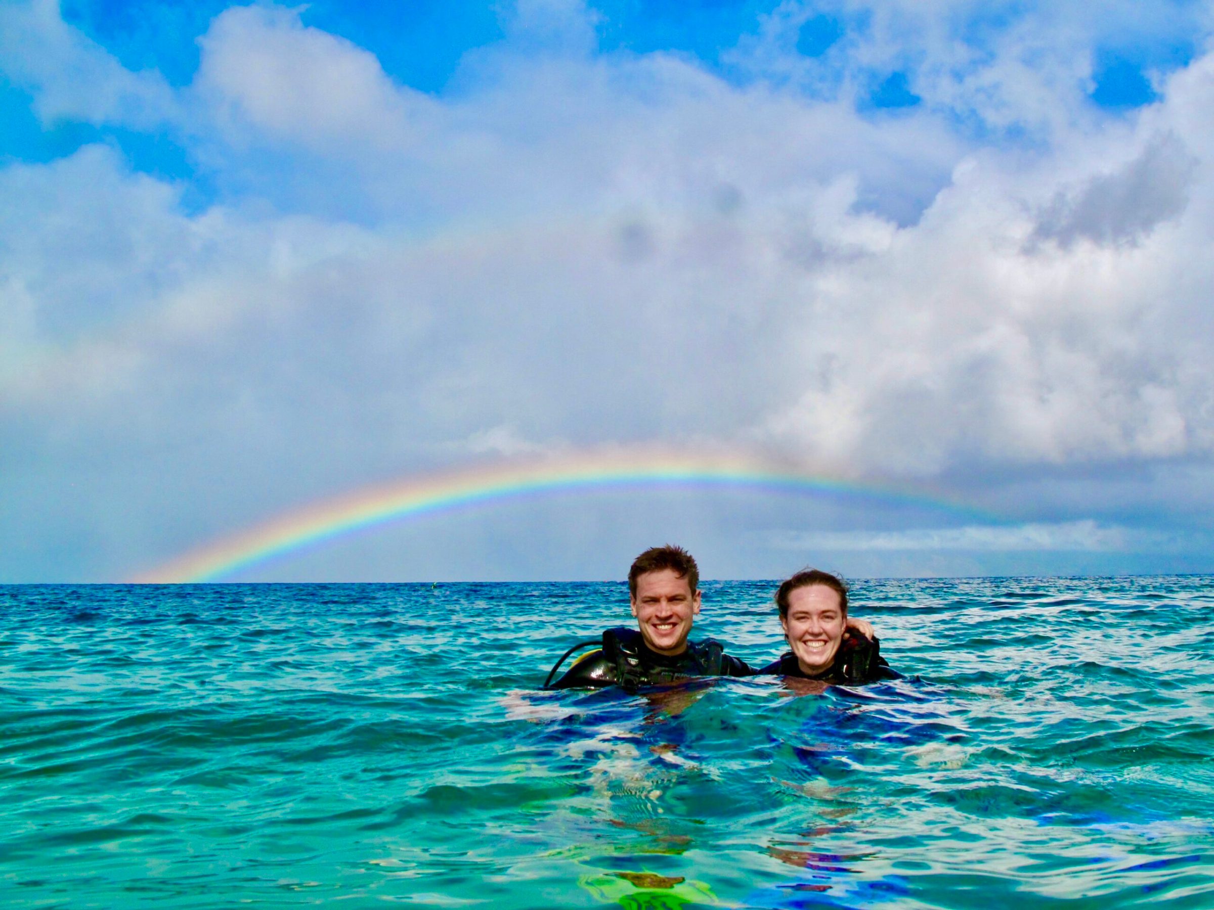 private scuba divers floating on the surface under a rainbow