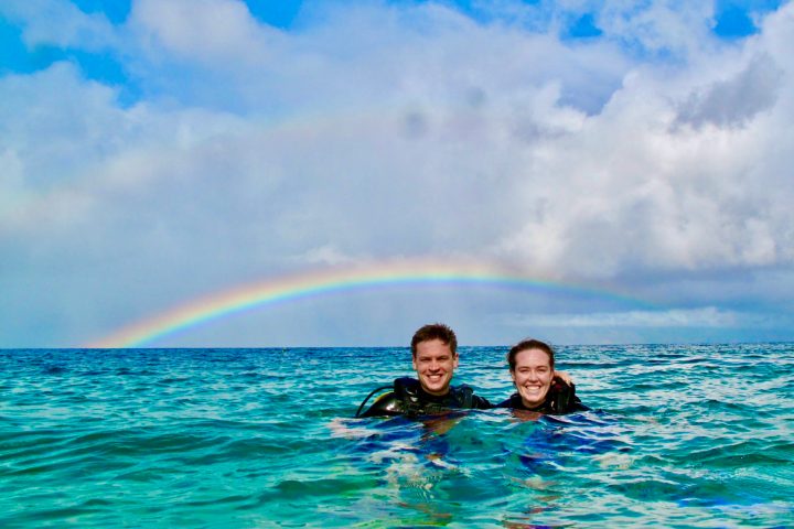 private scuba divers floating on the surface under a rainbow