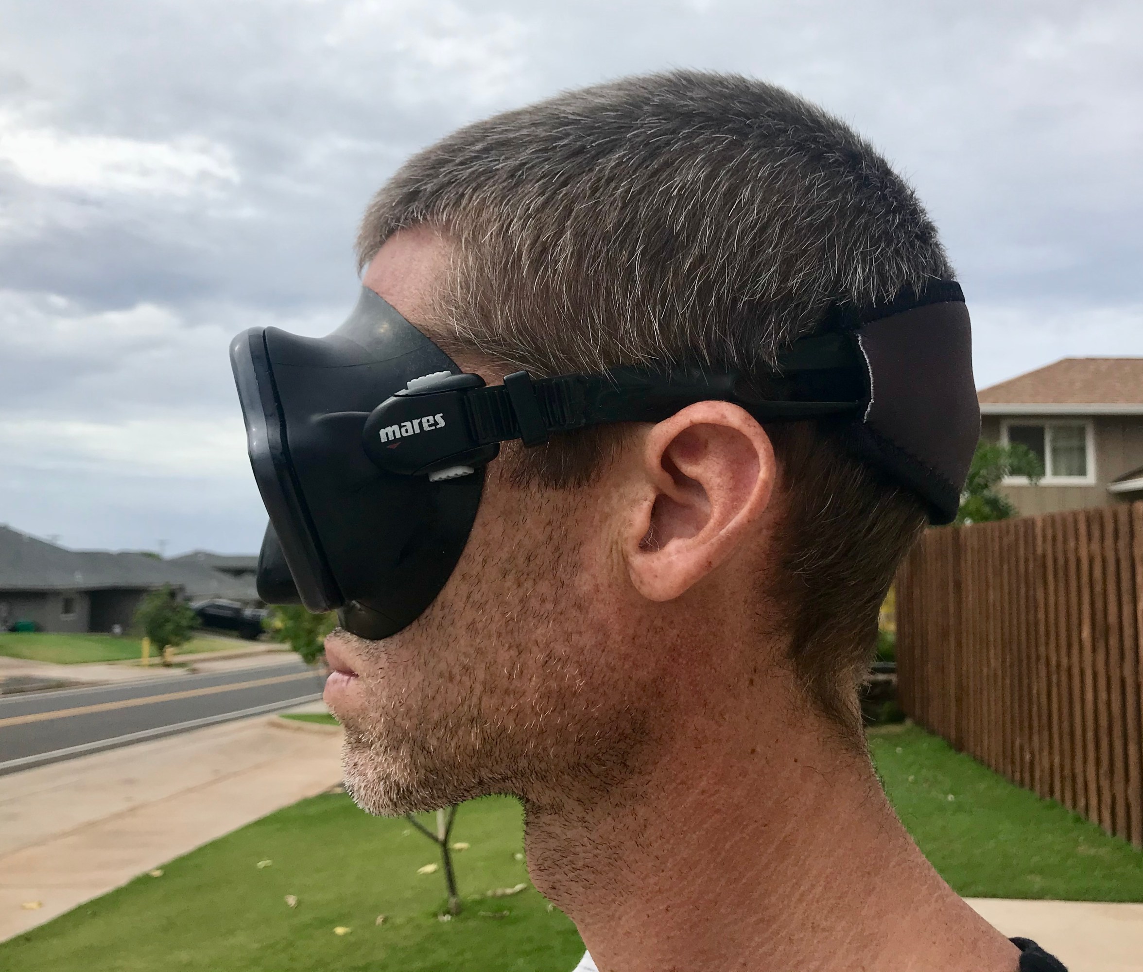 Side view of a person wearing a black scuba mask with the strap sitting above the ear and around the back of the head.