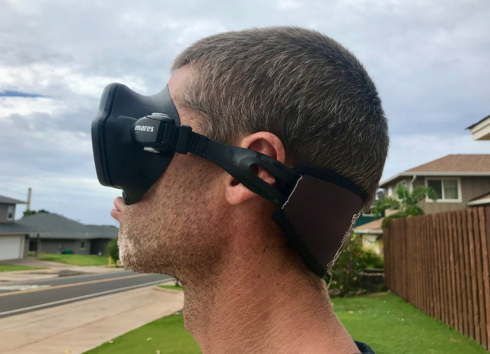 Side view of a person wearing a scuba mask with the strap crossing the ear and sitting low on the back of the head.